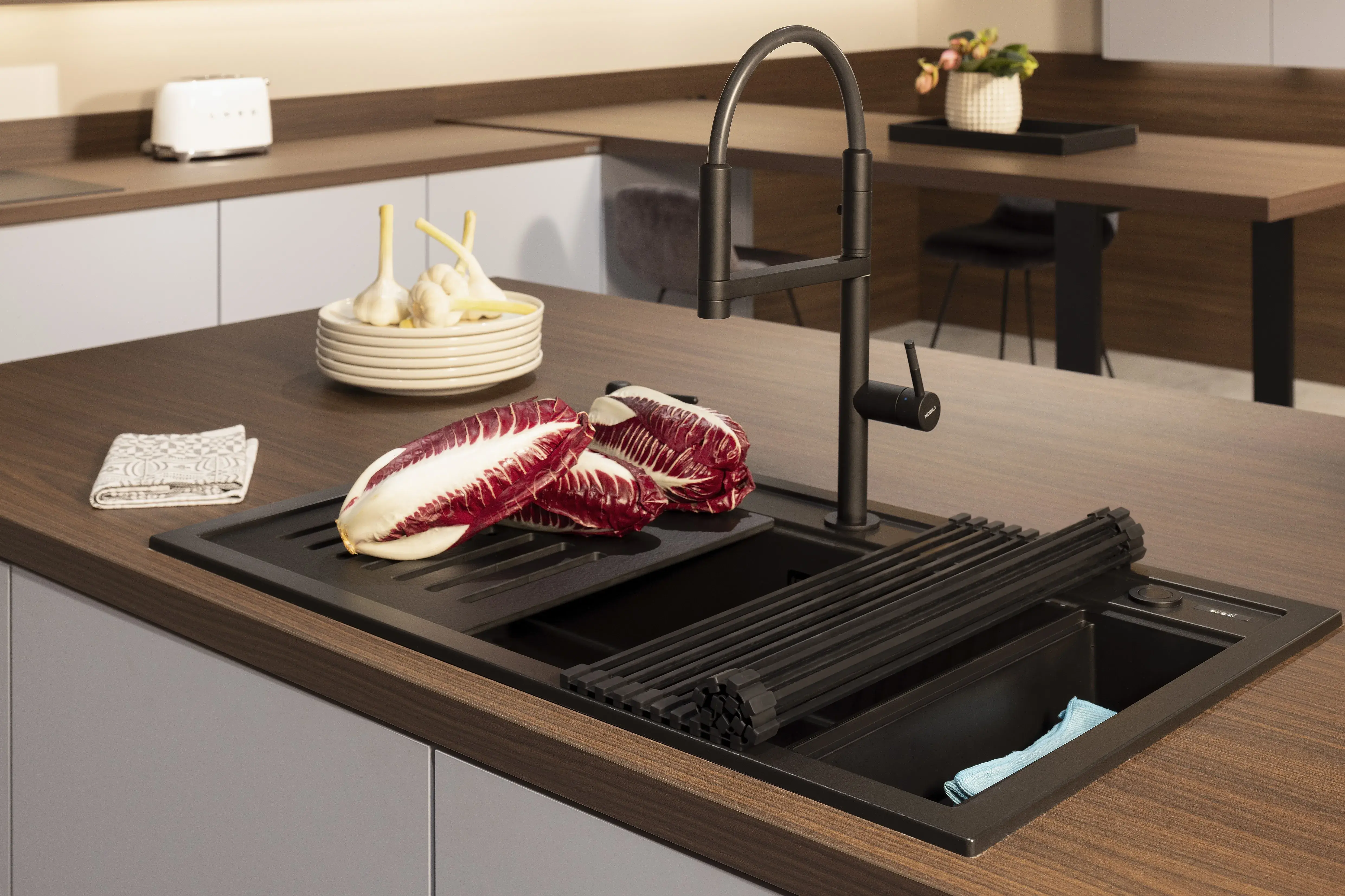 Moderne Küchenspüle mit dunklem Wasserhahn, Salat und Gemüse auf dem Abtropfgitter.